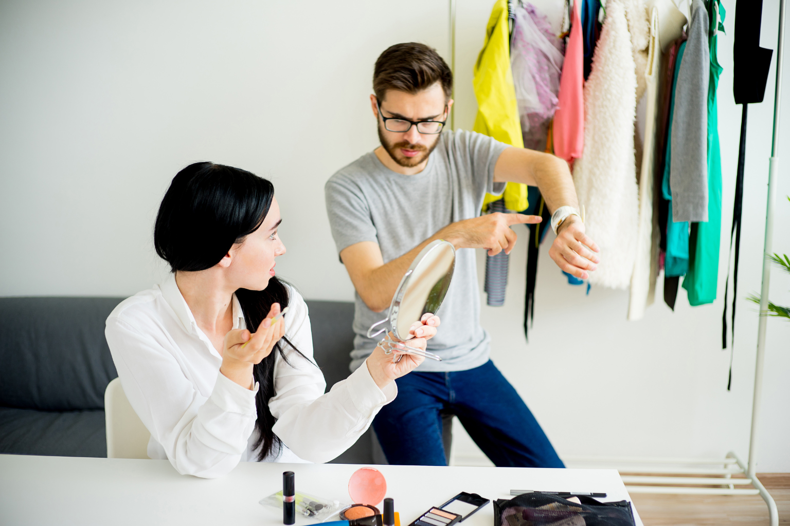 man showing his wife time on his watch while she is doing her make up