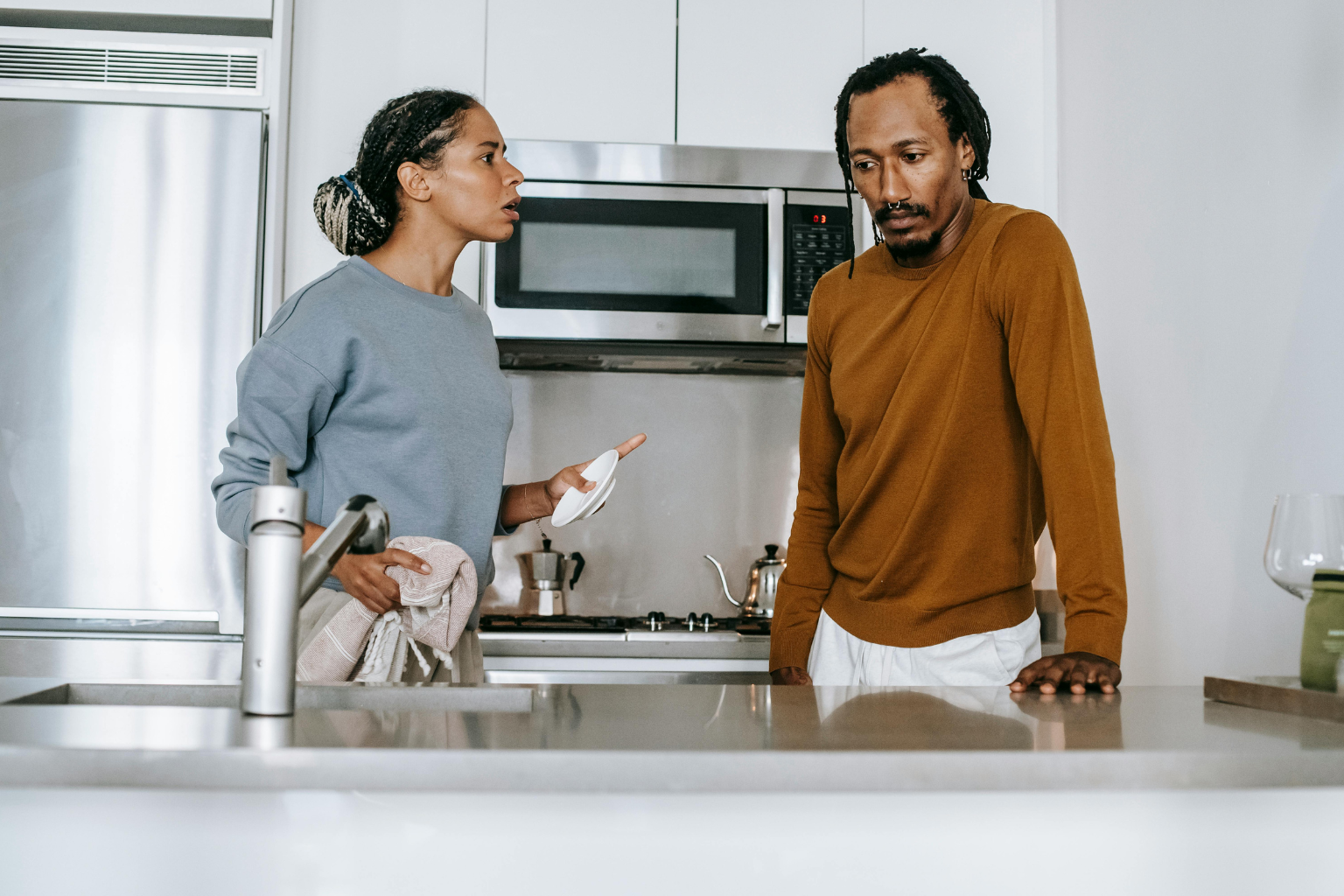 A wife with plate in her hand in the kitchen trying to have a conversation with husband. Husband looking away, trying not to engage in the conversation